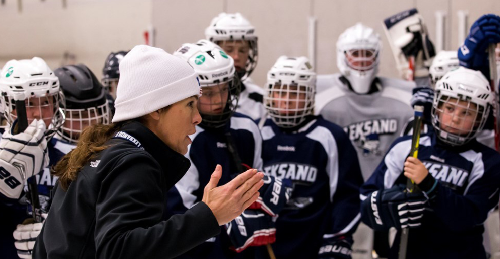 Kvinnlig tränare pratar med sitt ishockeylag. 