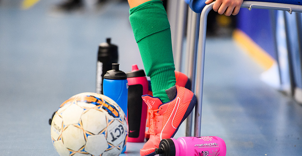 Barnfötter med orange fotbollsskor. Framför syns en fotboll. 