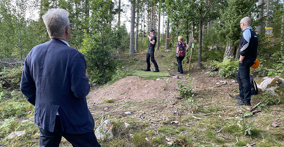 Björn står och tittar på när människor spelar discgolf i skogen
