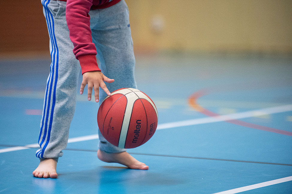 Ett barn studsar en basketboll inomhus i en idrottshall.