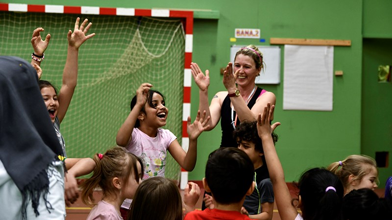 Tränare och barn skrattar och klappar händerna i en idrottshall. 