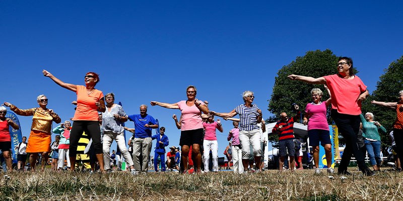 Seniorer tränar utomhus en varm sommardag. Himlen är blå och motionärerna har färgglada tröjor på sig. 